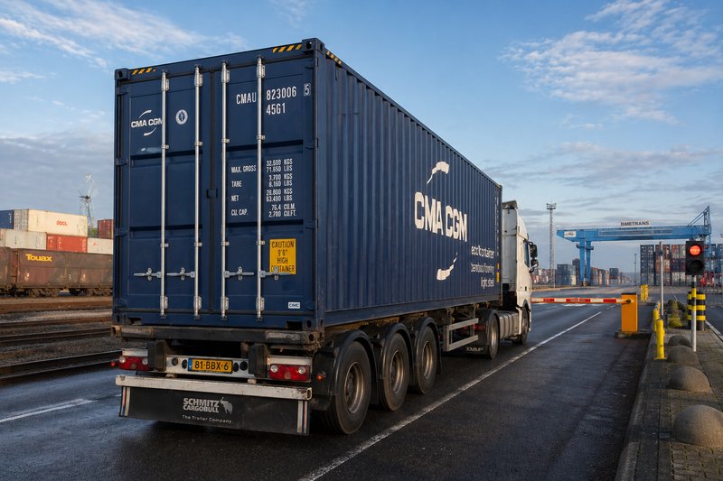 A truck loaded with a container is standing at the barrier on the access road to a container terminal.