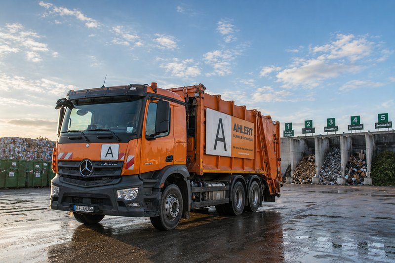 A dump truck stands ready in front of a pile of waste and recycling material.