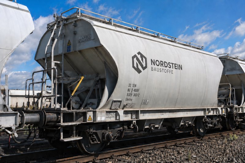 An open freight car loaded with gravel and a flat car loaded with cement bags are standing on a track.